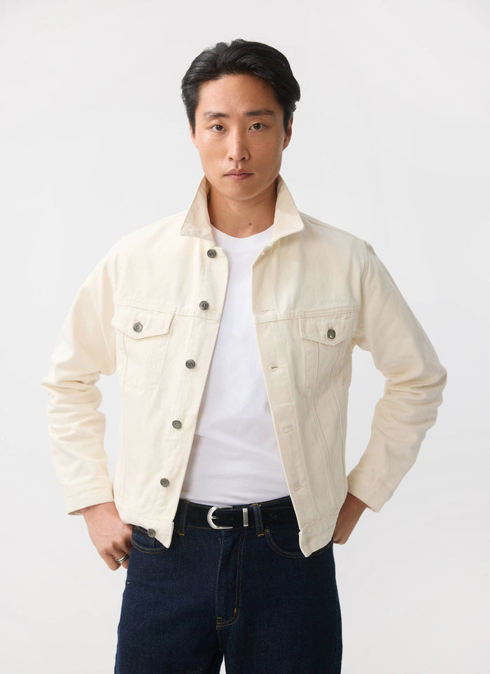 A man models the Percival ecru Western Trucker Jacket, styled open over a white tee and dark denim jeans.