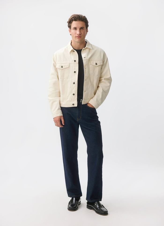 A male model wears the ecru denim Western Trucker Jacket from Percival, paired with dark jeans and a black t-shirt.