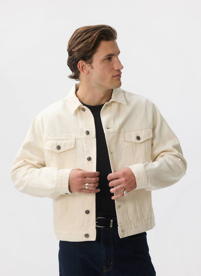 A model wears the ecru denim Western Trucker Jacket from Percival, styling it over a black t-shirt and jeans.