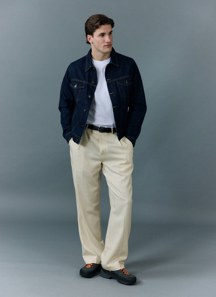 A model wears the Percival Western Trucker Jacket in indigo over a white tee with cream trousers, against a grey background.